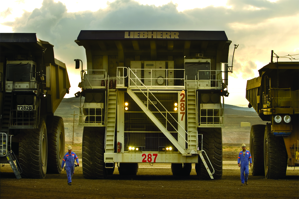 two miners walking by a haul truck